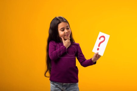 Photo for A portrait of thoughtful kid girl holding question mark card. Children, idea and knowledge concept - Royalty Free Image