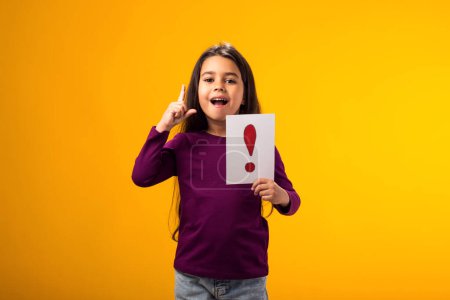 Téléchargez les photos : Portrait d'une gamine surprise tenant une carte de point d'exclamation et pointant du doigt. Enfants, idée et concept de connaissance - en image libre de droit