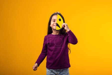 Photo for Portrait of smiling kid girl holding sad half face emoticon. Mental health, psychology and children's emotions concept - Royalty Free Image