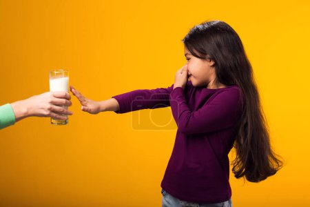 Foto de Retrato de niña con alergia a los lácteos que muestra stop gesture frente vaso de leche sobre fondo amarillo. Concepto de intolerancia a la lactosa - Imagen libre de derechos