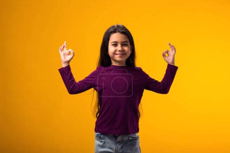 Photo for Portrait of smiling child girl looking through ok gesture over yellow background. Positive emotions concept - Royalty Free Image