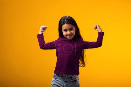 Téléchargez les photos : Portrait de gamine montrant gagnant ou geste de force sur fond jaune. Succès, victoire et bonne santé concept - en image libre de droit