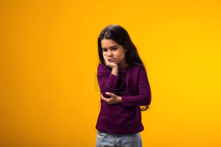 Téléchargez les photos : Portrait de fille triste tenant la joue avec la main se sentant déçu sur fond jaune. - en image libre de droit