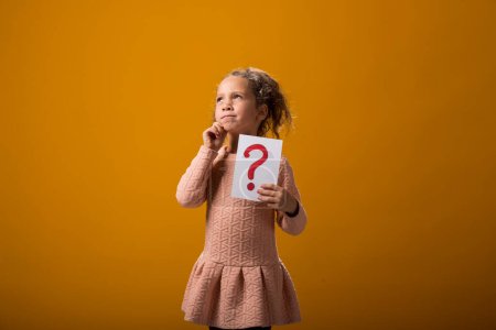 Photo for A portrait of thoughtful kid girl holding question mark card. Children, idea and knowledge concept - Royalty Free Image