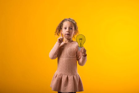 Photo for Portrait of surprised child girl holding paper bulb and pointing finger up. Success, motivation, winner, genius, idea concept - Royalty Free Image