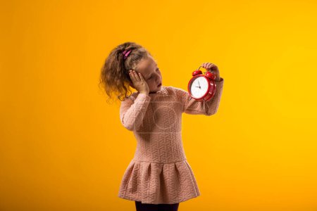 Photo for Portrait of surprised kid girl holding an alarm clock in hand. The concept of education, school, deadlines, time to study - Royalty Free Image