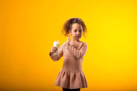 Foto de Retrato de niña con alergia a los lácteos sosteniendo un vaso de leche sobre fondo amarillo. Concepto de intolerancia a la lactosa - Imagen libre de derechos