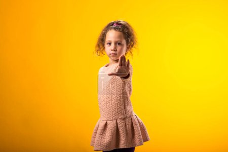 Téléchargez les photos : Portrait d'une enfant fille montrant un geste d'arrêt sur fond jaune. Bulling et concept des émotions négatives - en image libre de droit