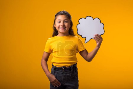 Foto de Retrato de niña sonriente sosteniendo tarjeta de burbuja de nube sobre fondo amarillo. Concepto de ensueño - Imagen libre de derechos
