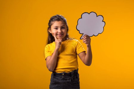 Photo for Portrait of thoughtful kid girl holding cloud bubble card over yellow background. Dreaming concept - Royalty Free Image