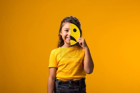 Photo for Portrait of smiling kid girl holding sad half face emoticon. Mental health, psychology and children's emotions concept - Royalty Free Image