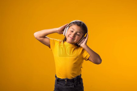 Photo for Portrait of smiling kid girl wearing pink dress enjoying music in headphones on yellow background. Lifestyle and leasure concept - Royalty Free Image