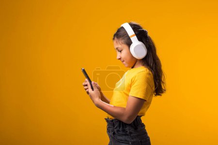 Téléchargez les photos : Portrait de fille souriante appréciant la musique dans des écouteurs sur fond jaune. Mode de vie, loisir et gadget concept de dépendance - en image libre de droit