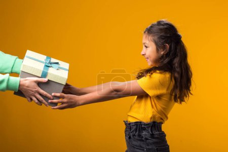 Foto de Retrato de niña sonriente aceptando caja de regalo sobre fondo amarillo. Cumpleaños y concepto de celebración - Imagen libre de derechos