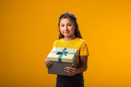Foto de Retrato de niña sonriente sosteniendo caja de regalo sobre fondo amarillo. Cumpleaños y concepto de celebración - Imagen libre de derechos