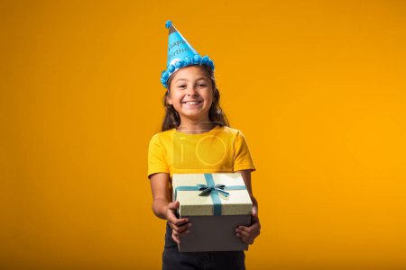 Téléchargez les photos : Portrait d'une jeune fille souriante tenant une boîte-cadeau sur fond jaune. Concept d'anniversaire et de célébration - en image libre de droit