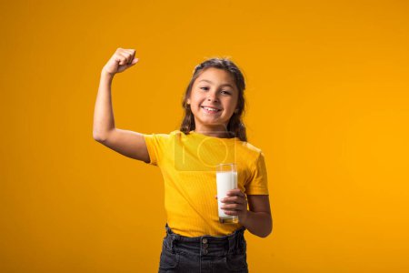 Téléchargez les photos : Portrait d'une enfant souriante tenant un verre de lait et montrant un geste tendu. Concept nutrition et santé - en image libre de droit