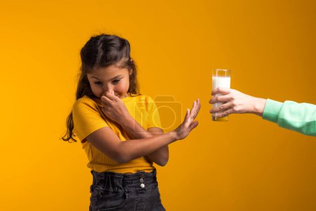 Foto de Retrato de niña con alergia a los lácteos que muestra stop gesture frente vaso de leche sobre fondo amarillo. Concepto de intolerancia a la lactosa - Imagen libre de derechos
