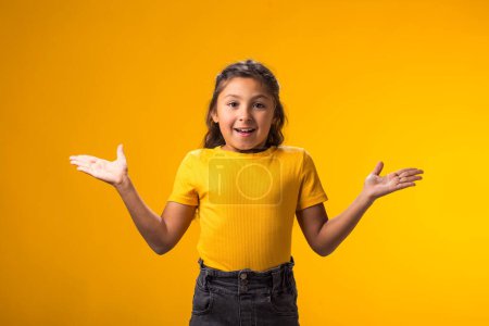 Foto de Retrato de una niña emocionada sosteniendo las manos sobre un fondo amarillo. Concepto de emoción - Imagen libre de derechos