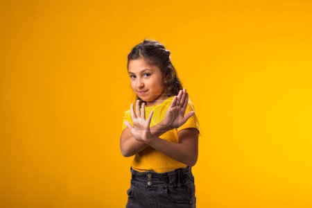Photo for Portrait of child girl showing stop gesture on yellow background. Bulling and negative emotions concept - Royalty Free Image