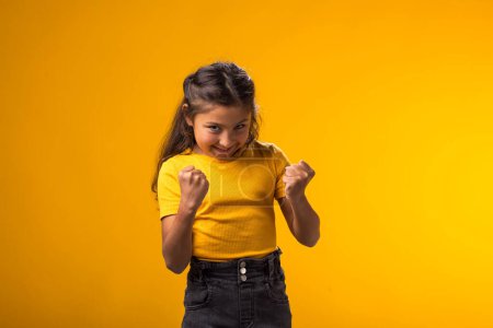 Foto de Retrato de niña enfurecida mostrando el puño en la cámara sobre fondo amarillo. Concepto de emociones negativas - Imagen libre de derechos