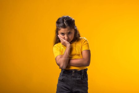 Téléchargez les photos : Portrait de fille triste tenant la joue avec la main se sentant déçu sur fond jaune. - en image libre de droit