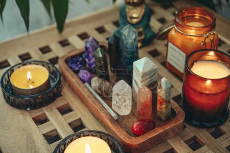 Verschiedene Mineralien und Heilkristalle auf einem hölzernen Tablett, Buddha-Statuette und Kerzen in Großaufnahme. Meditationskonzept. 