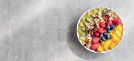 Photo for A healthy mango smoothie with blueberries, raspberries, kiwi and granola. Top view on light gray background. , copy space. - Royalty Free Image