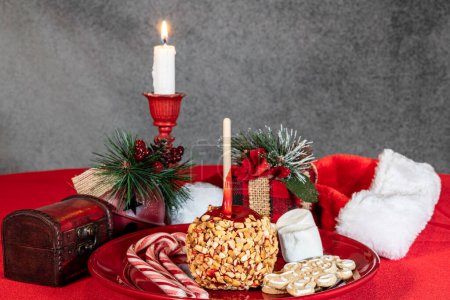 Foto de Dulces de Navidad bastones de caramelo de manzana pan de jengibre y malvaviscos en el plato rojo con velas ardientes y decoraciones navideñas - Imagen libre de derechos