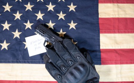 Foto de Guantes tácticos negros sosteniendo arma en la bandera americana con libertad no es nota libre - Imagen libre de derechos