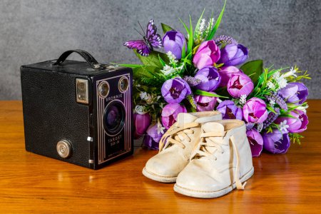 Foto de White leather baby shoes with vintage box camera on table with spring flowers - Imagen libre de derechos