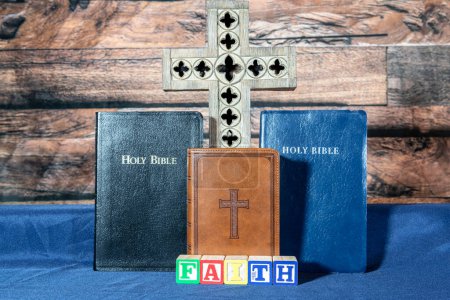 Photo for Three bibles and wooden cross on blue with wood blocks spelling faith - Royalty Free Image