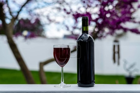 Photo for Bottle and glass of red wine on white rail outdoors with selective focus - Royalty Free Image