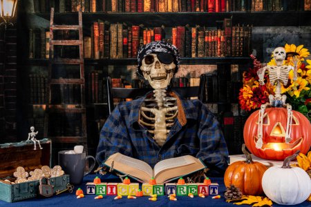 Foto de Libro de lectura esqueleto de Halloween en la biblioteca retro vestido como pirata con calabazas dulces galletas de maíz y jack-o-linterna - Imagen libre de derechos