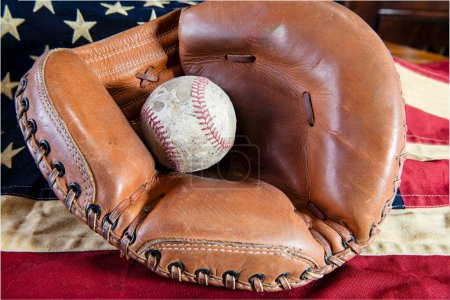 old worn baseball in leather catcher's mitt on tea stained American flag