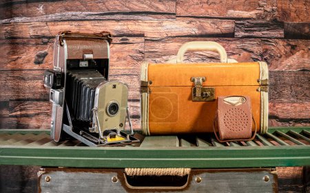 vintage camera and transistor radio with retro suitcase on green shutter and wood background