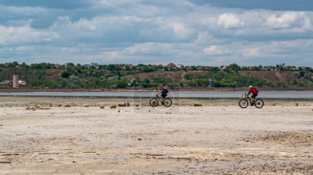 Photo for UKRAINE, KUYALNIK - MAY 23, 2021: two cyclists ride on the dried bottom of the Kuyalnik estuary - Royalty Free Image
