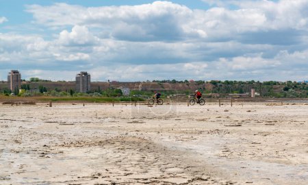 Photo for UKRAINE, KUYALNIK - MAY 23, 2021: two cyclists ride on the dried bottom of the Kuyalnik estuary - Royalty Free Image