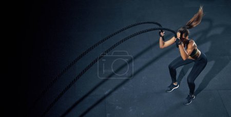 Foto de Ejercicio efectivo con una cuerda. Deportiva entrena en el gimnasio de entrenamiento funcional, realizando ejercicios de crossfit con una cuerda de batalla. - Imagen libre de derechos
