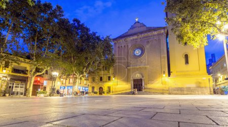 Foto de Barcelona, Spain - July 8, 2017: night view of Plaa de la Concrdia and Esglsia de Santa Maria del Remei with locals on benches in Barcelona, Spain. Les Corts used to be a town independent from Barcelona until the early 20th century - Imagen libre de derechos