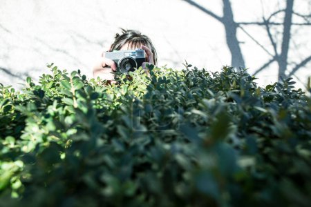 Photo for Woman shooting with vintage camera. Green bush - Royalty Free Image