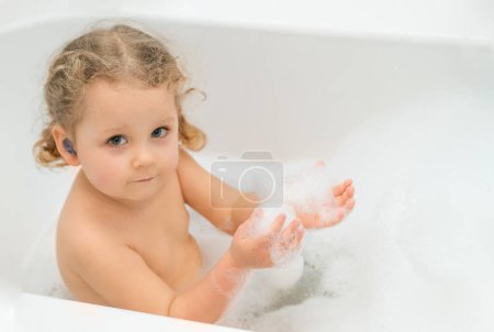 Photo for Earplugs for children, earplugs for swimming. A little girl is sitting in a bath with earplugs. Ear diseases in children. Protection against water ingress into the ears. - Royalty Free Image