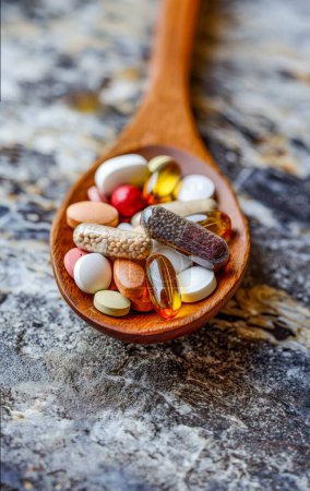 Assorted pharmaceutical medicine pills, tablets and capsules in wooden spoon.