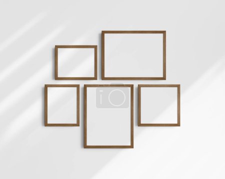 Foto de Conjunto de maquetas de pared Gallery, 5 marcos de madera de nogal marrón. Una maqueta moderna. Dos marcos horizontales, dos marcos verticales, y un marco cuadrado, 12x16 (3: 4), 16x12 (4: 3), 8x10 (4: 5), 10x8 (5: 4), 10x10 (1: 1) pulgadas, en una pared blanca con sombras. - Imagen libre de derechos
