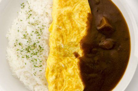 Riz au curry japonais garni d'omelette dans un plat blanc sur fond blanc.