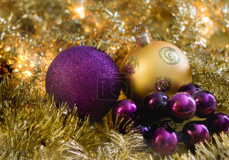 Photo for Purple and golden christmas baubles with golden garlands and glowing christmas lights in the background. - Royalty Free Image