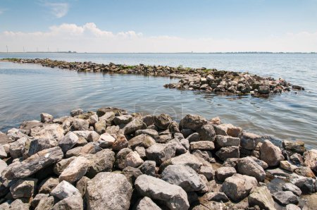 Große Felsbrocken bilden Wellenbrecher im Grevelinger See, um den kleinen Strand bei Battenoord in Goeree-Overflakkee in den Niederlanden vor den Wellen zu schützen.