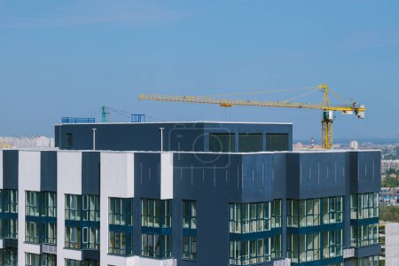 Photo for Top floor of  skyscraper. Construction site with yellow crane and building. Crane and building construction site against blue sky and city districts in the background. - Royalty Free Image