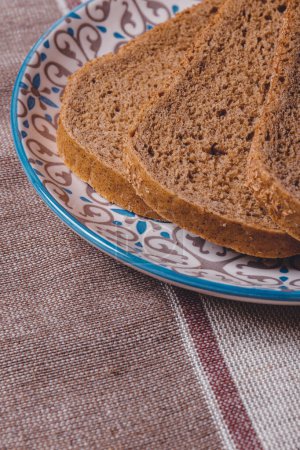 In Scheiben geschnittenes braunes Brot mit Kleie in einem Teller auf einer Tischdecke bedeckt.