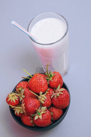 Téléchargez les photos : Bol noir aux fraises fraîches et milkshake froid aux fruits hachés en verre sur fond gris. - en image libre de droit